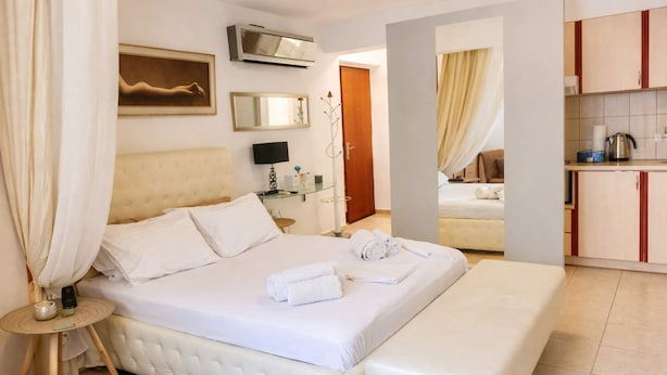 Ein Hotelzimmer mit einem großen Bett, einem Nachttisch, einem Fernseher, einem Spiegel und Blick zur Küche.