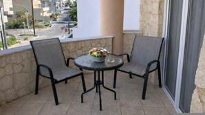 Un balcón con dos sillas, una mesa, un florero y vista a una calle y edificios.