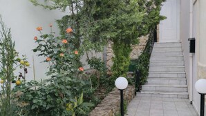 Un sendero en un jardín que lleva a una escalera, con un muro de piedra y plantas en macetas.
