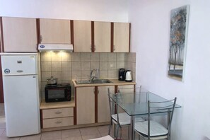 Een praktische keuken met een koelkast, magnetron, gootsteen en een glazen eettafel met stoelen.
