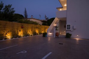 A modern building with a staircase leading to the entrance, a paved area with a 'P' marking, and a wooden fence with plants. - Diana s House 4 - Gytheio Sandy Beach Haven (East Mani)