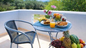 A balcony with a table set for breakfast, including fruits, bread, and a drink. - Diana s House 4 - Gytheio Sandy Beach Haven (East Mani)