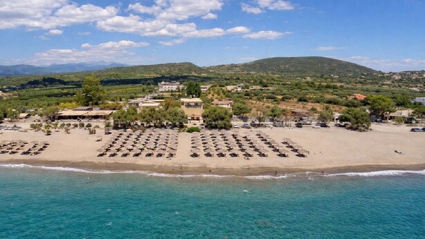 An aerial view of a beach with rows of sun loungers and umbrellas, a clear blue sea, and buildings in the background. - Diana s House 4 - Gytheio Sandy Beach Haven (East Mani)