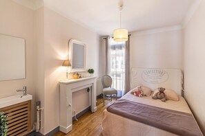 Une chambre à coucher avec un lit, une table de chevet avec une lampe, une chaise, une commode et une fenêtre avec des rideaux.