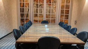 A conference room with a long table, black chairs, and large windows with autumn leaves.