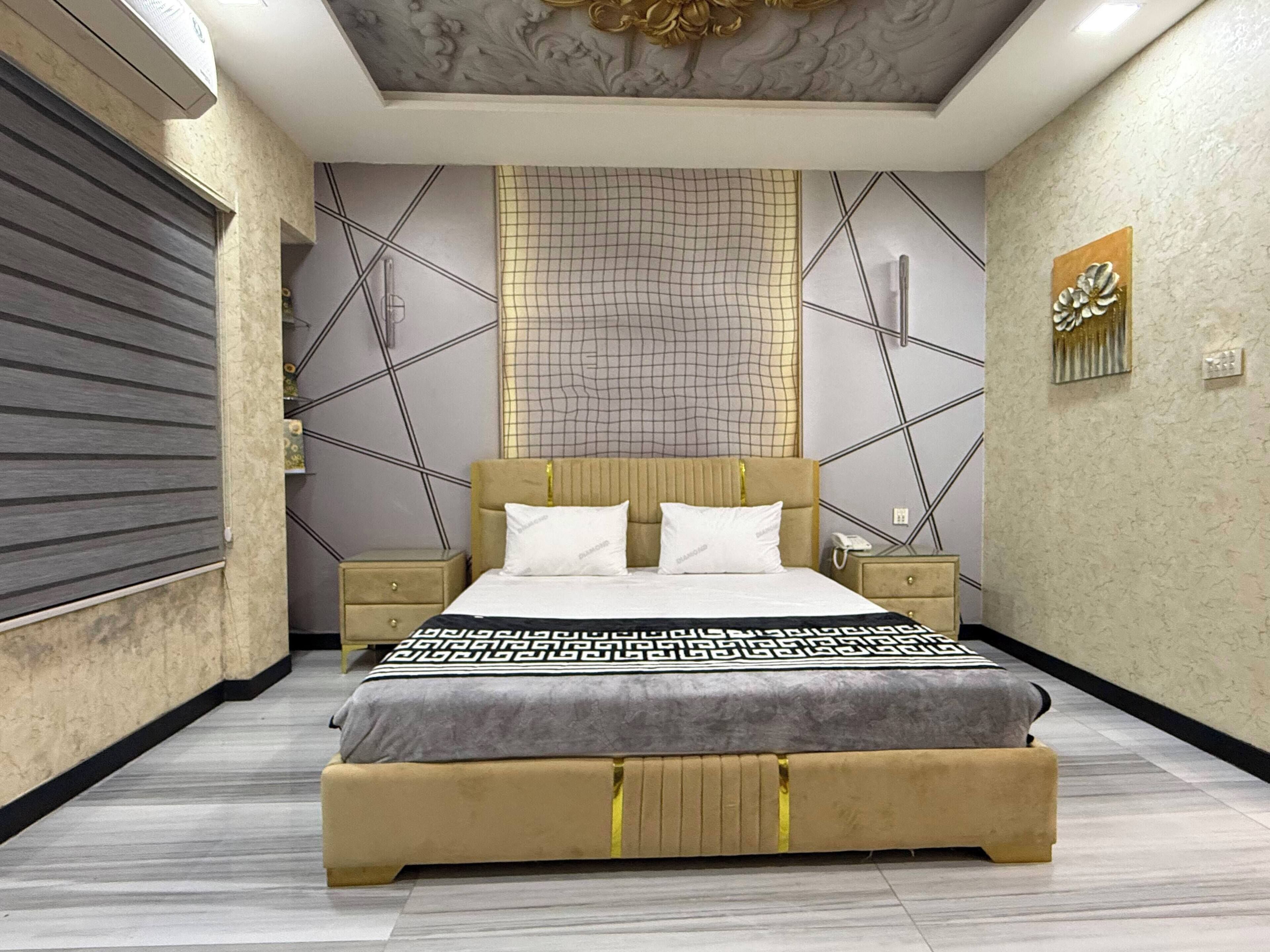 A modern bedroom with a large bed, two bedside tables, a decorative wall panel, and a ceiling with a geometric design.