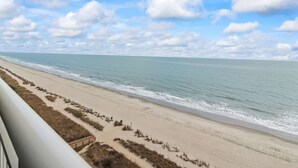 A beach view with a clear sky, sandy beach, and a wooden walkway leading to the water.