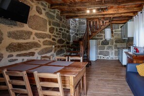 Ein rustikaler Raum mit Stehwänden, einem Holzespeisebereich mit Tisch und Stühlen, einer Treppe zu einer Küchenzeile und einem blauen Sofa mit gelbener Decke.