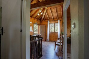 Ein Holzinnenraum mit hoher Decke, einer Treppe und Blick ins Freie.