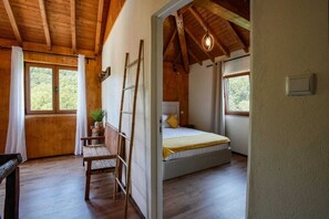 Ein Schlafzimmer mit Holzboden, einem Bett mit gelber Bettdecke, einem Holzstuhl und einer an der Wand angelehnten Leiter.