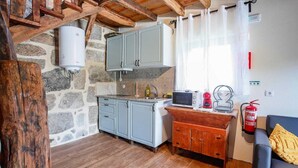 Una cocina compacta con armarios grises, una pared de piedra, techo de madera y un pequeño comedor con mesa y sillas.