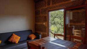 Una habitación acogedora con pared de piedra, un sofá azul oscuro con cojines naranjas y una mesa de madera con esteras.