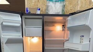 A refrigerator with multiple shelves and a freezer compartment, located in a room with a wooden wall and a visible cardboard box. - Pole Barn Style Lodge located at Reelfoot Lake accommodating to large groups! (Hornbeak)