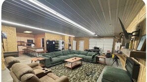A spacious living room with a sectional sofa, a small couch, and a coffee table. There is a kitchen area in the background with a refrigerator and a microwave. - Pole Barn Style Lodge located at Reelfoot Lake accommodating to large groups! (Hornbeak)