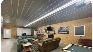 A spacious indoor area with a pool table, green sofas, and a dining area. - Pole Barn Style Lodge located at Reelfoot Lake accommodating to large groups! (Hornbeak)