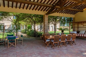 An outdoor patio with a wooden table and chairs, surrounded by brick flooring and greenery. - Villa 'La Vigna' with Private Pool, Wi-Fi and Air Conditioning (Gavorrano)