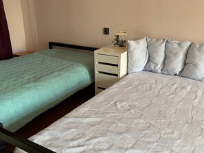 Un lit simple avec une couette blanche et une couette verte, une table de chevet agrémentée d’un petit objet décoratif, et un mur sobre.