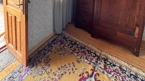 Una habitación con puerta de madera, un armario grande, un tapete estampado y una ventana con cortinas.