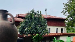 Un edificio rústico con techo de tejas rojas, un gran árbol en el patio y mesas al aire libre.