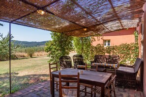 Une terrasse extérieure avec une table et des chaises, un toit de chaume et une vue sur un paysage verdoyant.