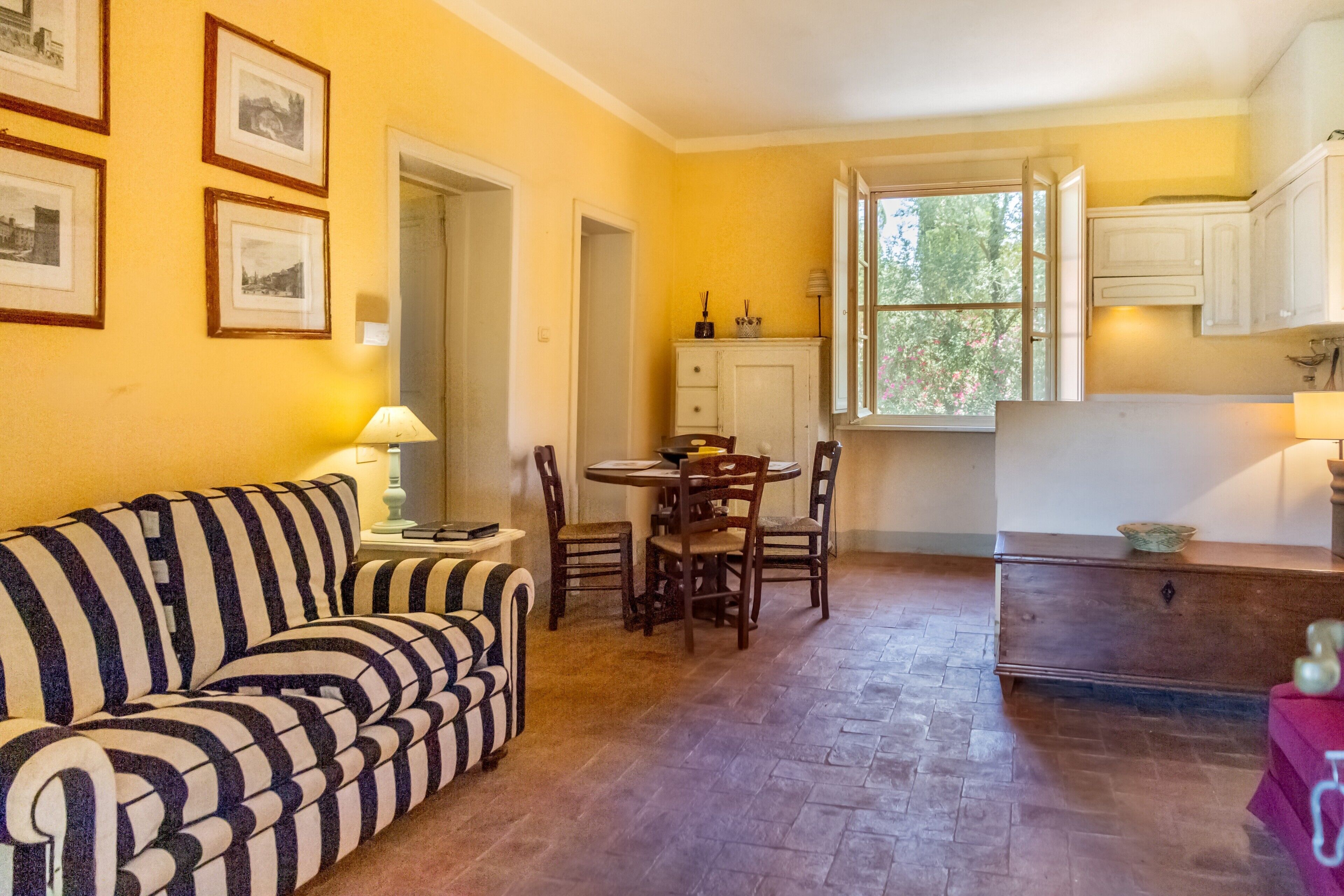Una habitación con un sofá a rayas, una mesa de comedor con sillas, una zona de cocina con armarios y cuadros en la pared.