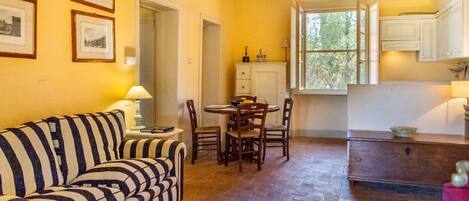Una habitación con un sofá a rayas, una mesa de comedor con sillas, una zona de cocina con armarios y cuadros en la pared.