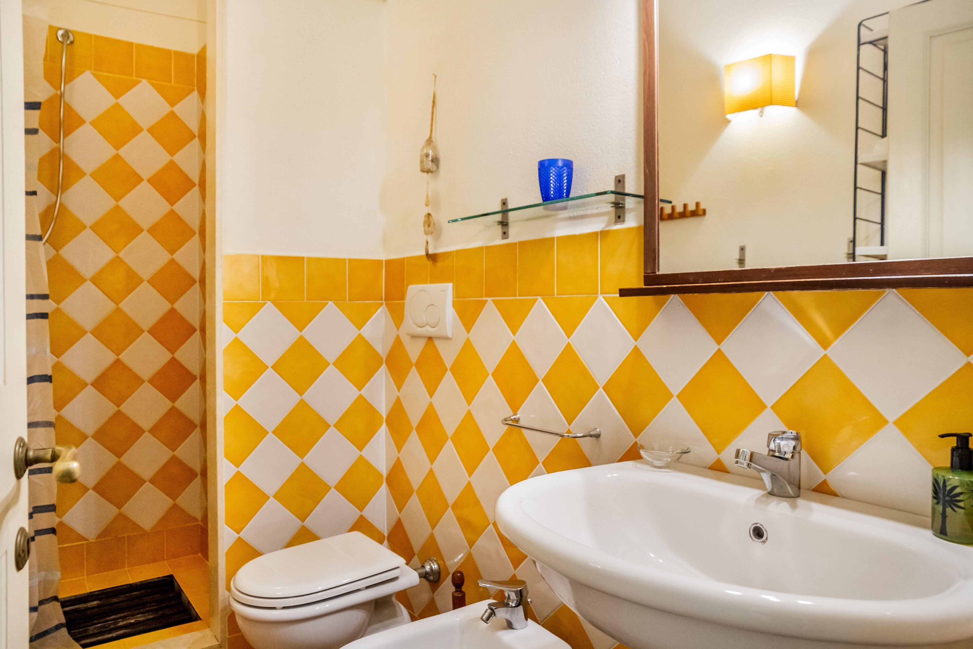 A bathroom with a white toilet, a white sink, and a shower with yellow and white tiles.