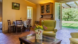 Una habitación con una mesa de comedor, sillas, un sofá, una mesa de centro de vidrio con un florero, un armario y una puerta corrediza de vidrio que da a un jardín.