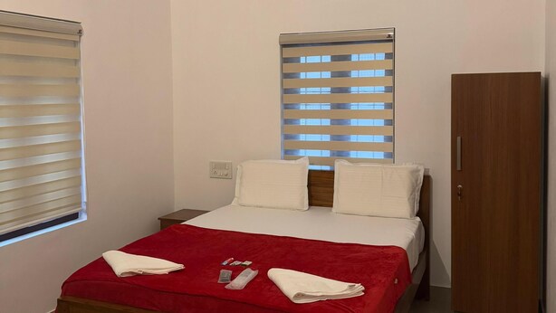 Une chambre d’hôtel avec un lit en bois, un ventilateur de plafond, un appareil de climatisation, une fenêtre avec des stores et une armoire.