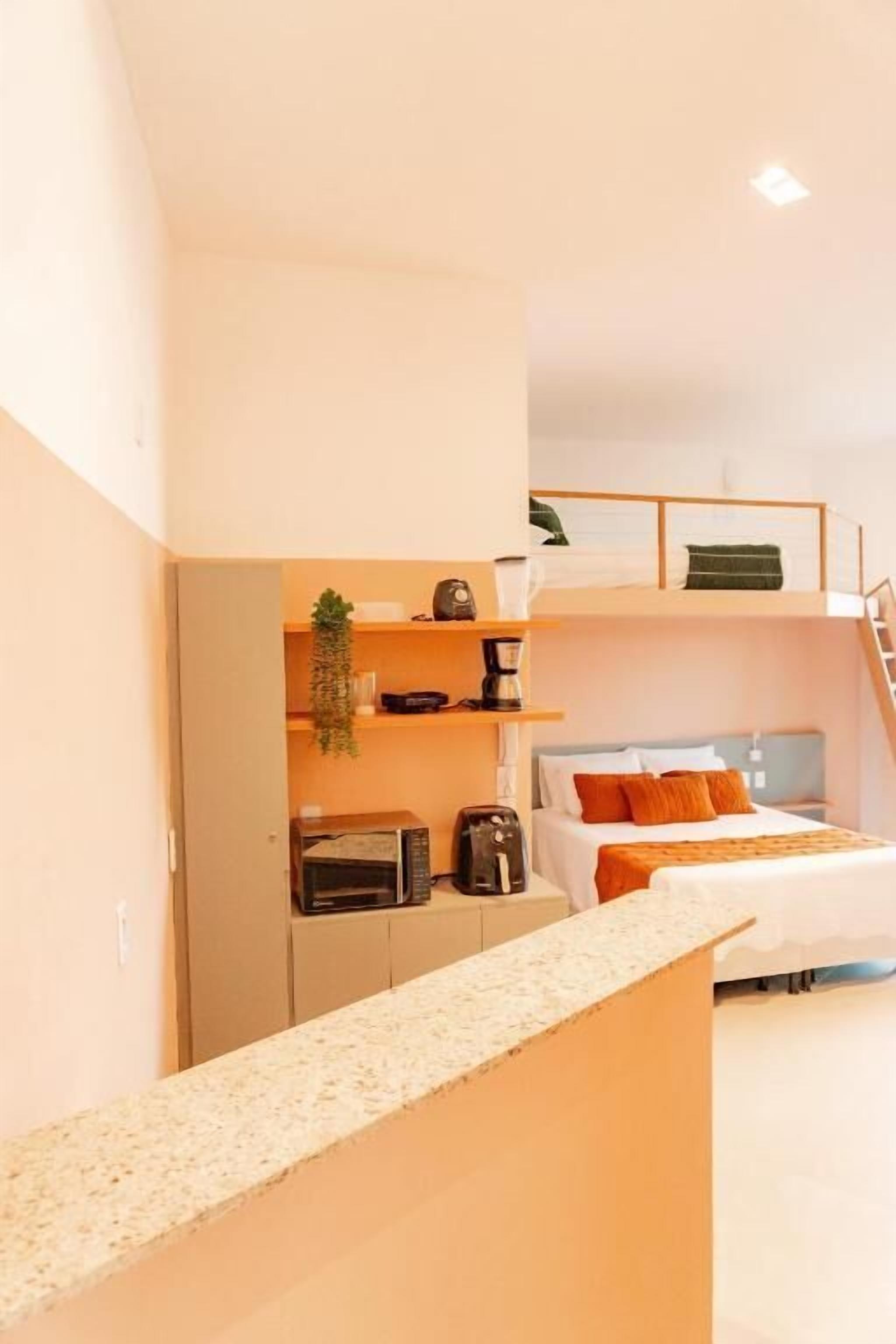 Una habitación compacta y moderna con literas, una kitchenette con cafetera y una planta pequeña.