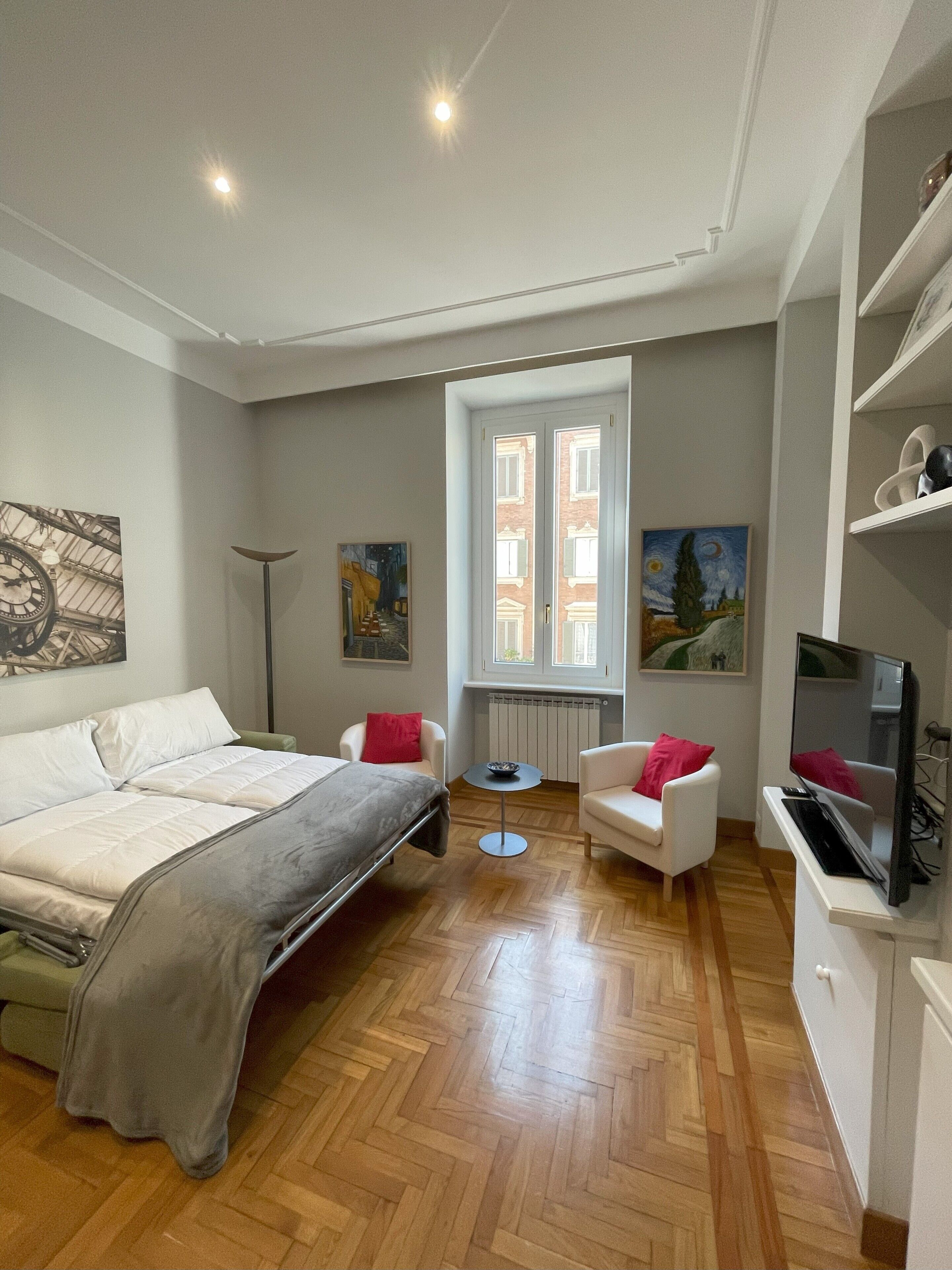 A bedroom with a bed, two chairs, a TV, and artwork on the walls.