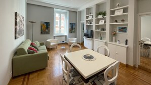 Moderni olohuone, jossa on ruokailutila, sohva, televisio ja hyllyjä, joissa on erilaisia esineitä.