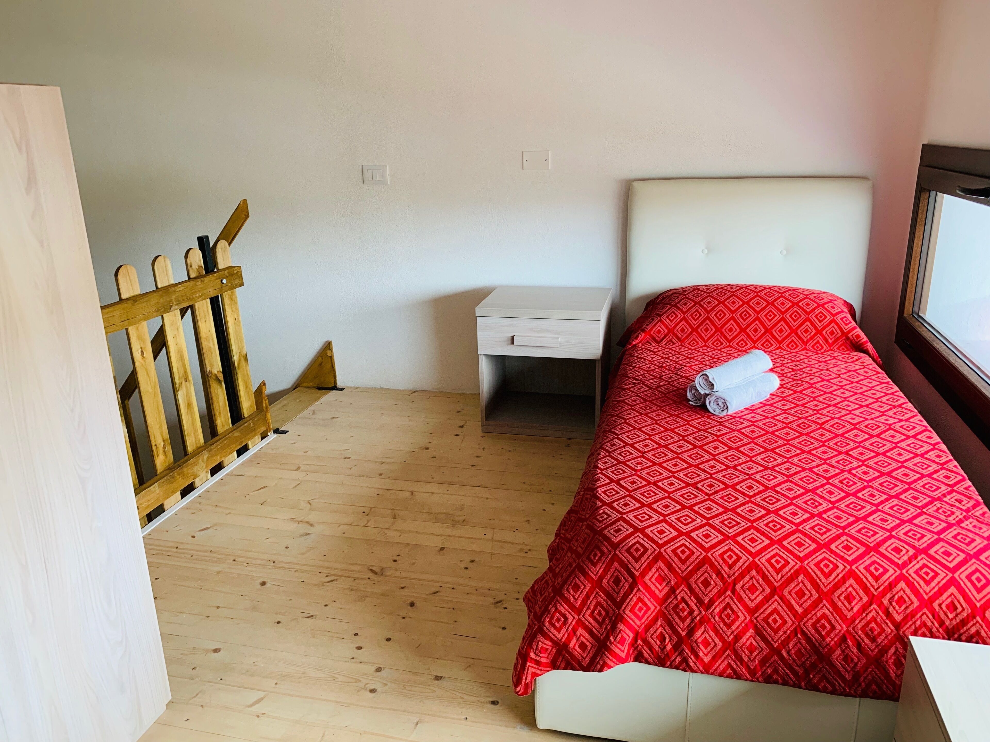 A small, neatly arranged room with a bed, a nightstand, and a wooden floor.