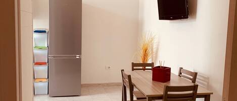 Una cocina compacta con refrigerador incorporado, una mesa de comedor con sillas y un televisor montado en la pared.