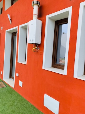 Un edificio rosso con cornice della finestra bianca, una porta e un quadro elettrico bianco fissato al muro.