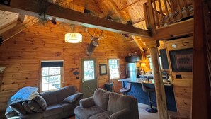 A cozy log cabin interior with a high ceiling, wooden beams, a fireplace, a dining area, and a sofa. - Log Cabin on the Clarion River! The Dam Inn 1 mile, 5 miles to East Branch Dam (Wilcox)