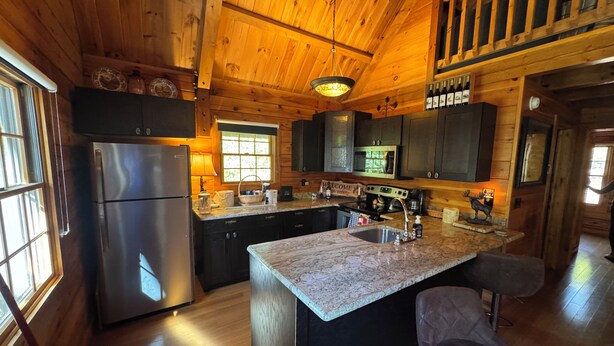 A modern kitchen with wooden walls, a granite countertop, stainless steel appliances, and a large island with bar stools. - Log Cabin on the Clarion River! The Dam Inn 1 mile, 5 miles to East Branch Dam (Wilcox)