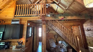 A rustic cabin interior with a wooden staircase, a kitchen area, and a cozy seating space. - Log Cabin on the Clarion River! The Dam Inn 1 mile, 5 miles to East Branch Dam (Wilcox)