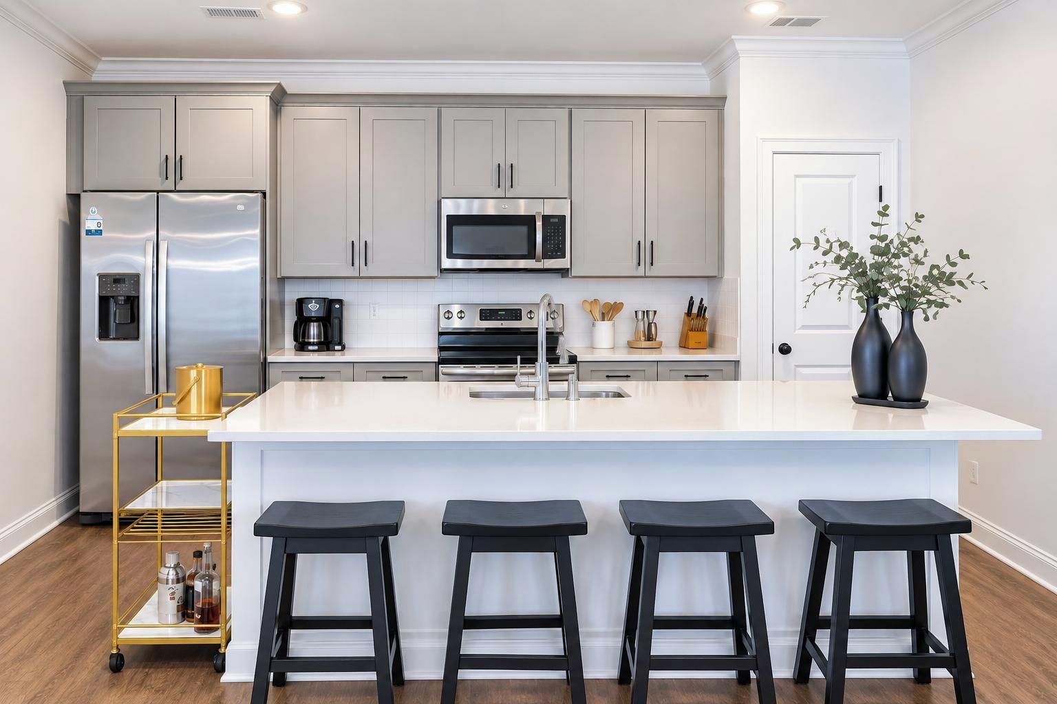 Una cocina moderna con electrodomésticos de acero inoxidable, una encimera blanca y taburetes de bar.