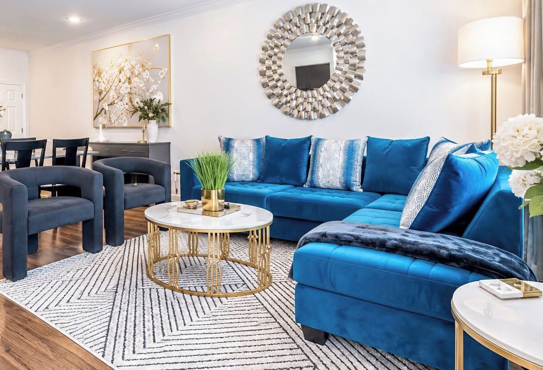 Een moderne woonkamer met een blauwe zithoek, een ronde salontafel en een eethoek met stoelen.