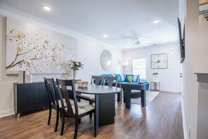 A modern dining area with a round table and chairs, a decorative wall piece, and a sofa in the background. - The Swayze, 3BR Retreat by Velvet Ditch Villas (Oxford)