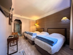 Quarto de hotel com duas camas, uma escrivaninha e uma cadeira.