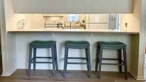 A kitchen with white cabinets, a countertop, and three stools. - Cozy 4BR Beach House Retreat (Bethany Beach)