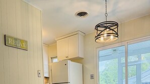 A dining area with a wooden table and chairs, a hanging light fixture, and a view of the outdoors through a glass door. - Cozy 4BR Beach House Retreat (Bethany Beach)