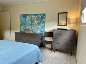 Ein Schlafzimmer mit einem Bett, zwei Kommoden, einem Sessel, einem Gemälde und einem Spiegel.