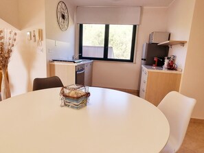 A compact kitchen with a dining area, a window with blinds, and a decorative vase on the table. - Splendid Sea View between Milazzo and Messina Facing Aeolian Islands (Sicilia)