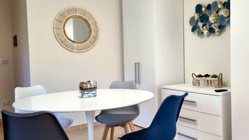Un'area pranzo moderna con un tavolo bianco rotondo, due sedie blu, un armadietto bianco e un elemento decorativo a parete.