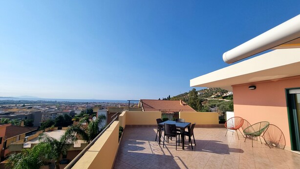 A balcony with a table and chairs, a view of the city, and a hillside in the background.