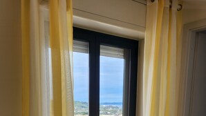 A room with a sliding glass door leading to a balcony with a view of the sea.