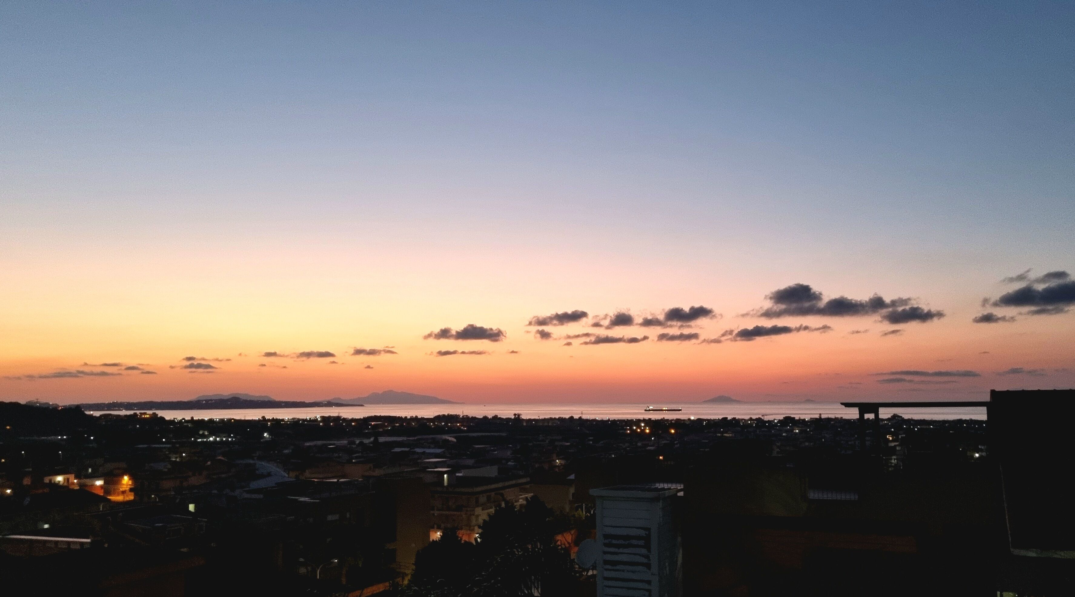 A cityscape at dusk with a clear sky and distant mountains.